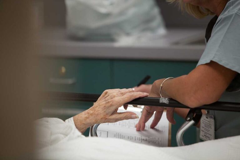 An older adult reading with a staff member in a comfortable, home-like community lounge.